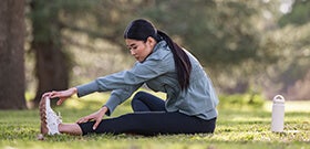Adult woman sitting on grass outdoors, stretching