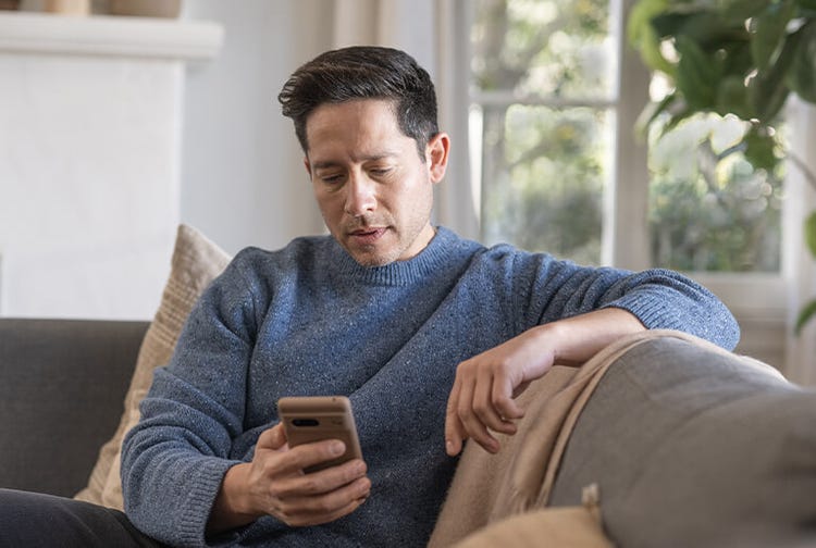 Adult man indoors looking at mobile phone on a sofa