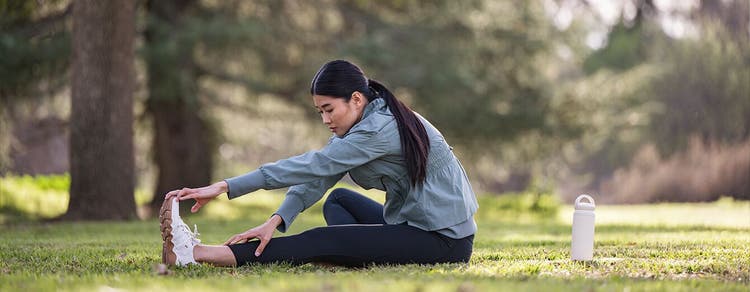 Adult woman sitting on grass outdoors, stretching