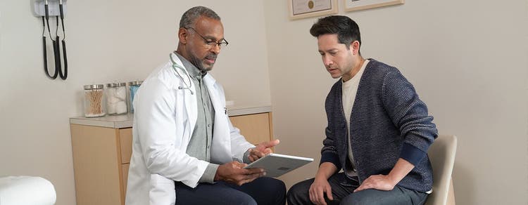 Adult male patient in exam room discussing with his physician looking at tablet