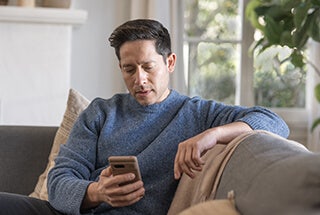 Adult man indoors looking at mobile phone on a sofa