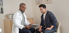 Adult male patient in exam room discussing with his physician looking at tablet