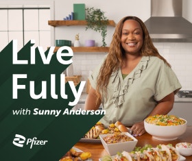 Smiling Sunny Anderson standing at a kitchen counter filled with food dishes