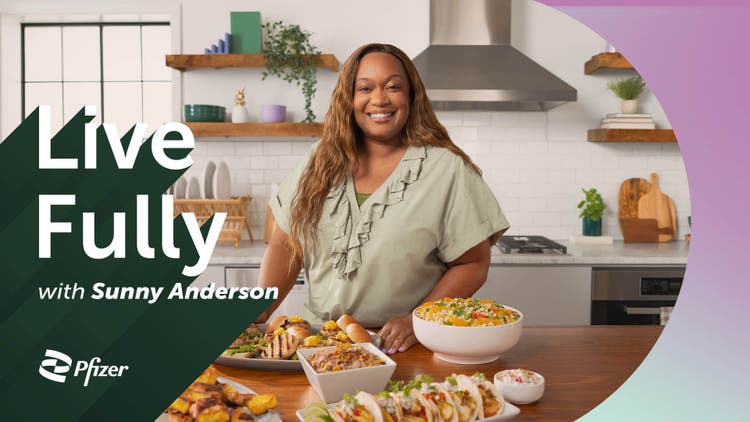 Smiling Sunny Anderson standing at a kitchen counter filled with food dishes