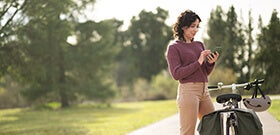 Adult woman outdoors beside bicycle using mobile phone