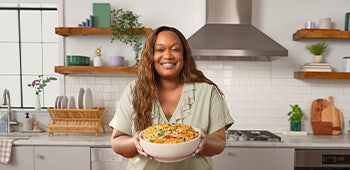 Sunny Anderson standing at kitchen counter holding a bowl of food