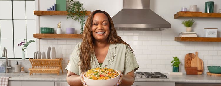 Sunny Anderson standing at kitchen counter holding a bowl of food