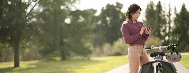 Adult woman outdoors beside bicycle using mobile phone