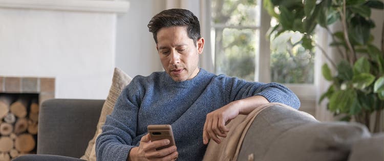 Adult man indoors looking at mobile phone on a sofa